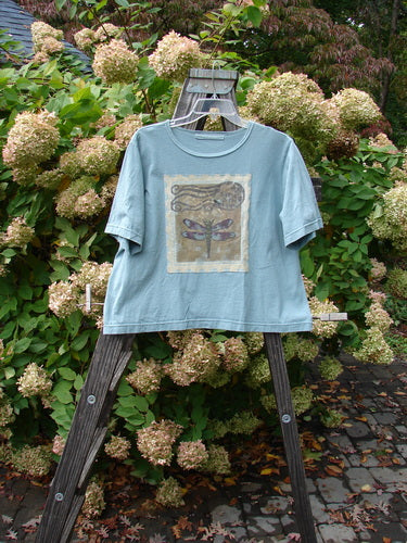 1999 Patched Short Sleeved Crop Tee Dragonfly Stream Size 1 displayed on a wooden easel, showcasing its dragonfly-themed patch and feminine rolled neckline.