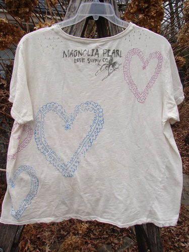 Magnolia Pearl NWT Cotton Jersey Boyfriend Tee Frida Del Sol True OSFA features a soft, drapey feel with scalloped-edge heart designs and Magnolia Pearl branding on the back, hanging outdoors.