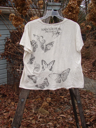 Magnolia Pearl NWT Cotton Jersey Boyfriend Tee Beyond Butterflies True OSFA displayed outdoors, featuring black butterfly illustrations and distressed details, draped over wooden frame amidst a rustic backdrop.