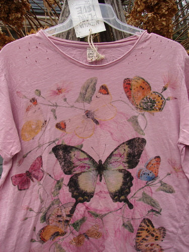 Magnolia Pearl NWT Cotton Jersey Boyfriend Tee Profound Responsibility Allium OSFA features a butterfly and floral print on light-pink fabric, with artistic distressing and unique seam design, hanging on a clear hanger.