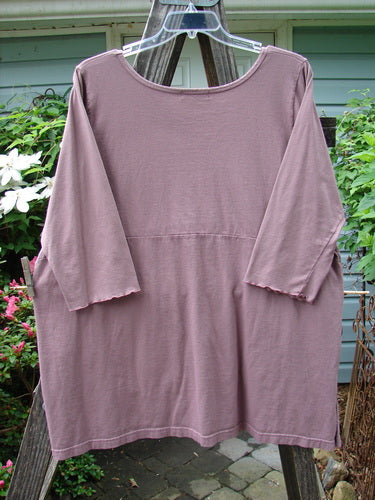 Barclay Empire Vented Pocket Top Unpainted Dusty Plum Size 2 displayed on a clothes rack, showcasing its rounded neckline, tall vented sides, two exterior drop pockets, and three-quarter length sleeves.