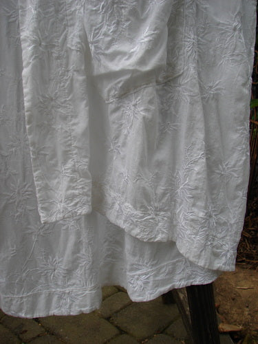Close-up of Barclay Brocade Open Front Pocket Dress Duster, showcasing silken floral vine pattern, open front with drop pockets, and varied hemline. White, size 2, from Blue Fish Clothing's Holiday Collection.