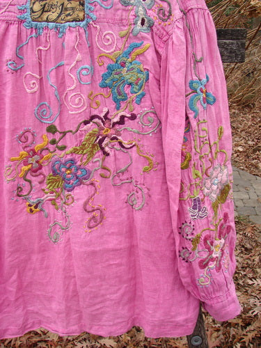 Magnolia Pearl Embroidered Linen Gypsy Johnny & Co Shirt Pinkster OSFA, featuring vibrant floral embroidery, a relaxed fit, wide neckline, and billowy sleeves, hanging outdoors against a rustic backdrop.