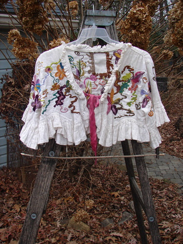 Magnolia Pearl Embroidered Linen Ruffle Ribbon Bolero White OSFA draped on a wooden ladder, showcasing ruffled tiers, colorful floral-vine embroidery, and pink ribbon tie, embodying Bluefishfinder.com's vintage aesthetic.