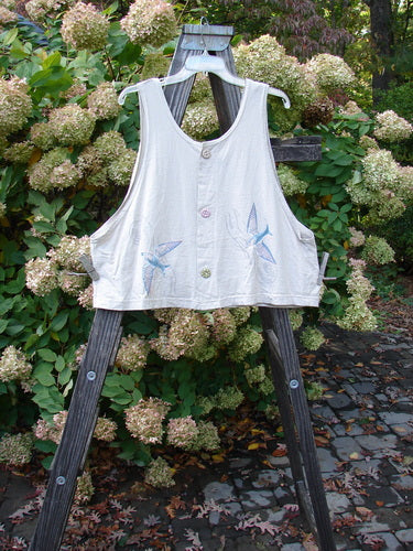 1999 Pinwheel Vest Love Dove Dust Size 2 displayed on a wooden stand, features bird-themed paint, three front buttons, and a slightly flared hemline, made from organic cotton.
