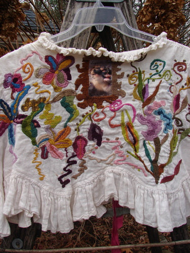 Magnolia Pearl Embroidered Linen Ruffle Ribbon Bolero White OSFA featuring vibrant hand-embroidered floral and abstract designs, scalloped ruffles, and a stitched animal face patch, showcasing a bohemian, artistic aesthetic.