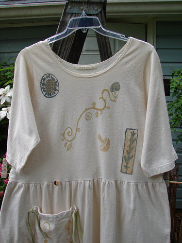 1994 Flower Garden Dress Sun Garden Tea Dye Altered Size 2: White shirt with whimsical sun garden design, featuring a scooped neckline, drop waist seam, generous fabric folds, and a repositioned pocket.