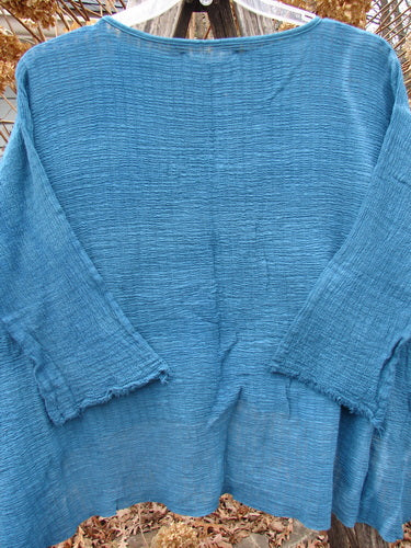 Barclay NWT Crinkle Gauze Top in Mottled Teal OSFA, featuring a loose, textured design with a high-low hemline, three-quarter dolman sleeves, and a shallow neckline, hanging outdoors.