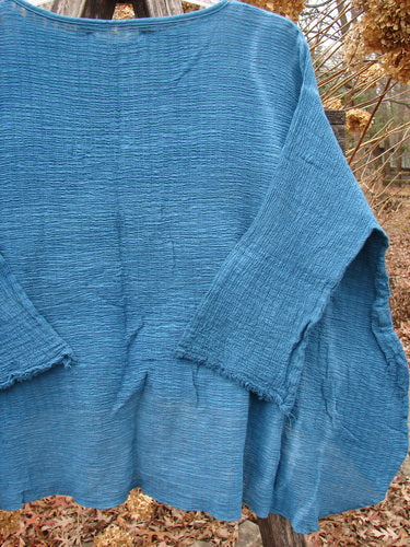 Barclay NWT Crinkle Gauze Top Mottled Teal OSFA, featuring a loose, forgiving fit with three-quarter dolman sleeves, a high-low hemline, and a shallow neckline, displayed against a rustic outdoor backdrop.