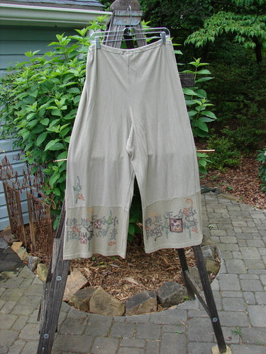 Barclay Cotton Hemp Drawstring Cuff Bottom Pant in Wheat, hanging on a clothes line, showcasing a wide, paneled bottom with detailed Asian-inspired painted accents.