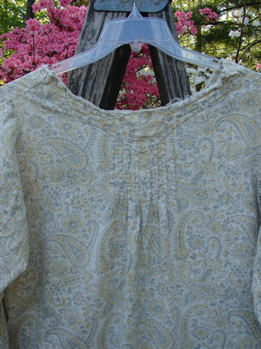 Magnolia Pearl NWT European Cotton Bondi Blouse Fleuri OSFA hangs on a clear plastic hanger, showcasing its raw-edged V-neckline, billowy three-quarter sleeves, and intricate paisley print against a rustic backdrop.