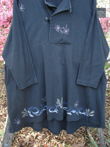 1997 Rhadha Dress Star Flowers Trail Obsidian Size 2, featuring a loose A-line shape with hand-painted floral motifs, mock stand-up collar, and deep side pockets, displayed against a backdrop of flowering shrubs.