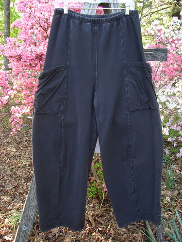 Barclay Interlock Cuff Toboggan Pant Unpainted Black Size 1 displayed outdoors on a hanger, showcasing its loose fit, large cargo-style side pockets, fleece cuffs, and vertical stitch detailing.