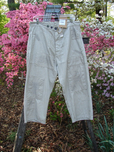 Magnolia Pearl NWT European Denim Lilou Trouser Natural Pinstripe OSFA displayed outdoors, showcasing its patch pockets, adjustable button fly, and unique distressed detailing against a floral shrub backdrop, highlighting creative individuality.
