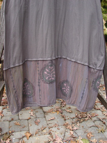 Barclay Pleated Banded Bottom Sweep Dress in Mushroom displayed on a wooden stand, featuring a pleated front neckline, sectional sleeves, double exterior pockets, and detailed fern graphics.