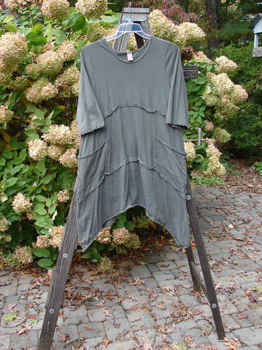 Barclay Cotton Lycra Raw Edge Vector Pocket Tunic Dot Grey Green Size 1 displayed on a wooden rack with three-quarter sleeves, drop wrap side pockets, and a varying hemline.
