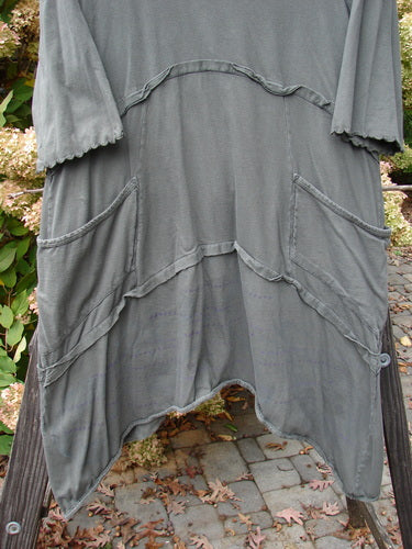 Barclay Cotton Lycra Raw Edge Vector Pocket Tunic Dot Grey Green Size 1 displayed on a wooden pole, featuring three-quarter sleeves, a varying hemline, and two exterior pockets.