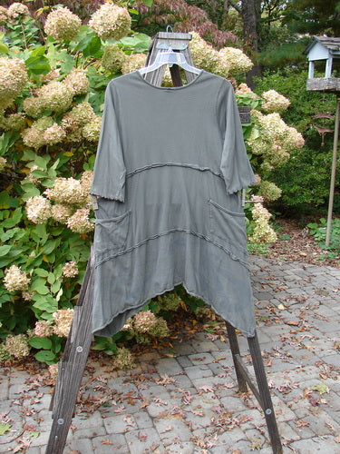 Barclay Cotton Lycra Raw Edge Vector Pocket Tunic Dot Grey Green Size 1 displayed on a wooden stand, showcasing three-quarter sleeves, varying hemline, and two drop wrap side pockets.