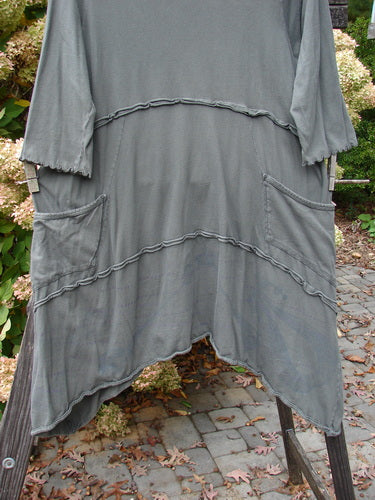 Barclay Cotton Lycra Raw Edge Vector Pocket Tunic Dot Grey Green Size 1 displayed on a rack, showcasing its three-quarter sleeves, flutter accents, varying hemline, and two side exterior pockets.