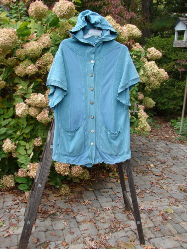 Barclay Celtic Moss Hooded Pocket Cardigan Unpainted Dusty Aqua Size 0 displayed on a wooden stand, showcasing its short sleeves, hood, full button front, and two lower exterior pockets.