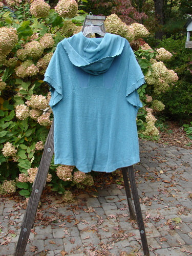 Barclay Celtic Moss Hooded Pocket Cardigan Unpainted Dusty Aqua Size 0 displayed on a wooden stand, featuring short sleeves, a floppy hood, two lower pockets, and curly edgings.