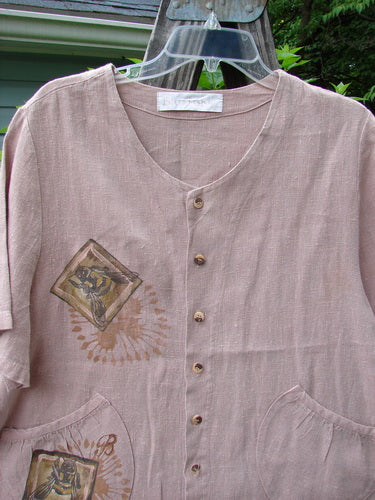 1998 Botanicals Robin's Top Bee Mallow Size 0: A pink shirt with garden-themed artwork, featuring a square illustration of a person, dual front pockets, and seven small buttons.