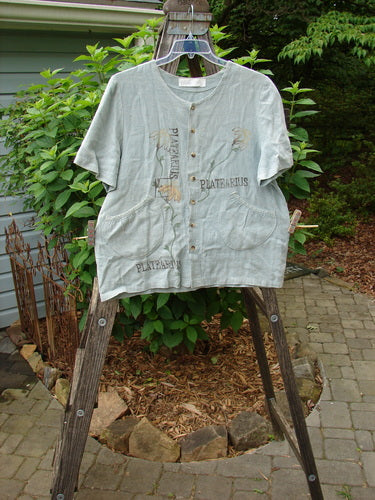 1998 Botanicals Robin's Top Platearius River Size 0 displayed on a wooden rack, highlighting its unique A-line shape, dual front elastic pockets, and seven tiny buttons, showcasing its vintage, artistic design.