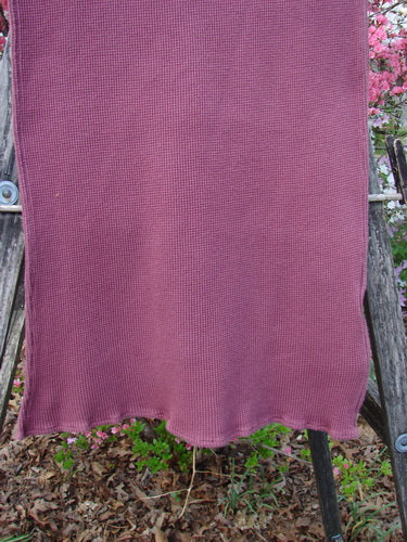 1992 Thermal Scarf Unpainted Mulberry OSFA draped on a wooden rack, showcasing its waffle texture and curly edges. The scarf is displayed outdoors with pink blossoms in the background, highlighting its cozy appeal.