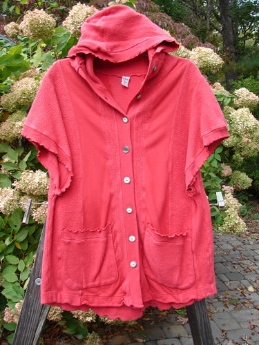 Barclay Celtic Moss Hooded Pocket Cardigan Unpainted Geranium Size 0 displayed on a fence, showcasing its floppy hood, short sleeves, button front, and exterior pockets.