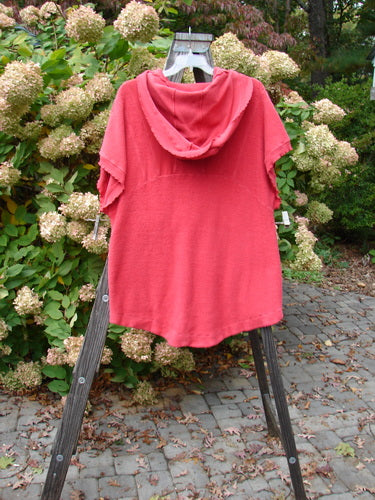 Barclay Celtic Moss Hooded Pocket Cardigan Unpainted Geranium Size 0 displayed on a wooden stand, showcasing its floppy hood, short sleeves, two pockets, curly edgings, and sectional fabrics.