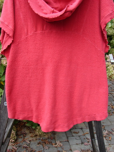 Barclay Celtic Moss Hooded Pocket Cardigan Unpainted Geranium Size 0 displayed on a wooden post, featuring short sleeves, a floppy hood, two exterior pockets, and a button front with textured fabric.