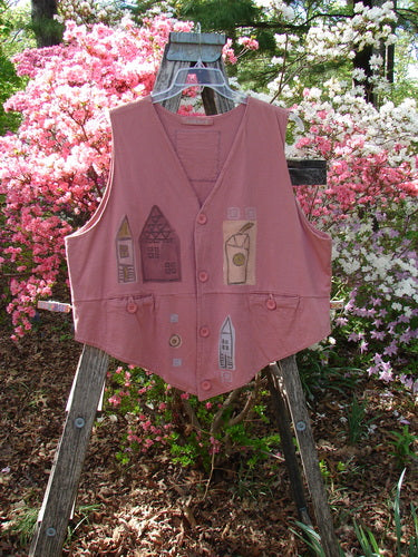 1995 Button Vest Village Russet OSFA, featuring a dusty-rose sleeveless design with stitched appliqués of houses and drinks, displayed on a wooden ladder amidst blooming shrubs, embodying vintage Blue Fish creativity.