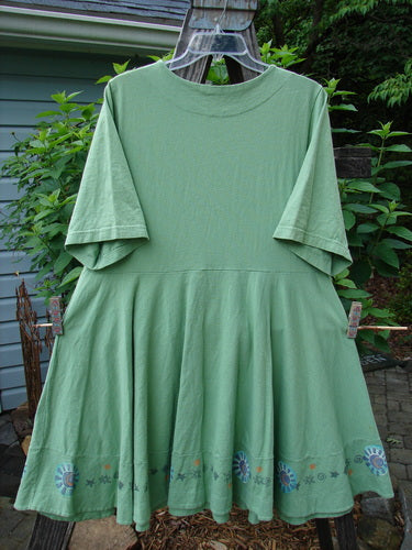 1999 Nest Dress Sun Border Spearmint Size 0 displayed on a clothes rack, showcasing its paneled neck, short sleeves, and swingy lower hem with a painted upper hip pocket.