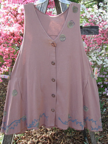 1993 Short Column Vest Floral Vine Rosewood OSFA: A rose-pink, sleeveless tunic with a V-neck, wooden buttons, and floral vine patterns, featuring a flared hem, displayed outdoors against a rustic wooden structure.