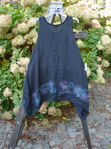 Barclay Linen Lace Pinafore Jumper Daisy Border Black Size 0 displayed on a wooden stand, showcasing a rounded neckline with lace accents and varying dip side hem, outdoors.