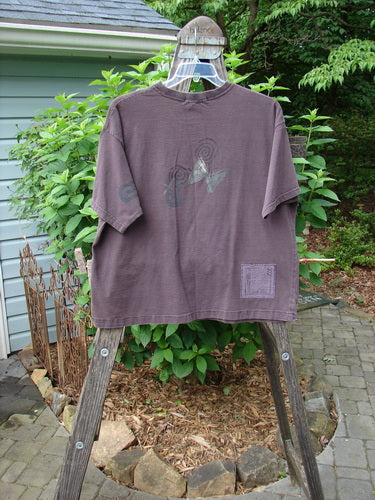 1995 Short Sleeved Tee Butterfly Madderlake Altered Size 2 displayed on a hanger, showcasing its drop shoulders and thicker ribbed neckline with a boxy, shorter fit and detailed paint design.