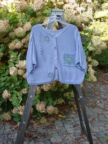 1995 Cotton Rayon Short Sleeved Cardigan Sweater Friendly Garden Dusk Mélange Size 3 displayed on a wooden rack, showcasing colorful buttons, varied textures, wide shape, and ribbed neckline.