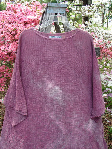 Barclay Crinkle Gauze Ana Tunic Dress Unpainted Mottled Rusty Rose OSFA on a hanger, showcasing its loose fit and textured fabric with wide sleeves, set against a floral garden backdrop.