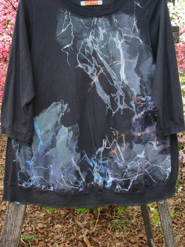 Barclay Flutter Edged Essential Tee Lightning Black Size 1 hangs on a wooden frame, showcasing its bleach-splattered design and raw-edged mesh neckline with three-quarter sleeves, exemplifying Bluefishfinder.com's vintage style.