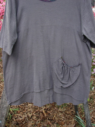 Barclay Gauze Contrast Ditsy Daisy Pocket Top Unpainted Stone Size 1, loose-fit slate-gray with floral neckline accents, textured knit, elbow-length sleeves, round neckline, gathered pocket, draped over a wooden chair outdoors.