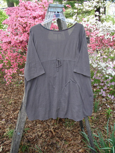 Barclay Gauze Contrast Ditsy Daisy Pocket Top Unpainted Stone Size 1, loose-fitting with ¾ sleeves, drawstring waist, and floral accents, displayed outdoors against flowering shrubs on a wooden trellis.