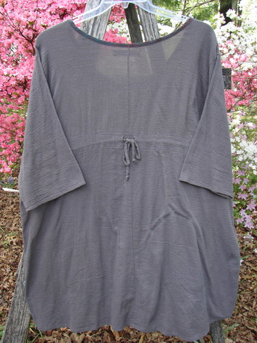 Barclay Gauze Contrast Ditsy Daisy Pocket Top in stone displayed on a rustic ladder. Features include a three-quarter sleeve, drawstring waist, and distinct floral-patterned neckline and pocket.