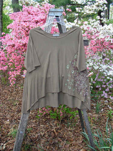 Barclay Hi Low Top Side Art Curly Cue Bark Size 1 features a loose-fitting design with elbow-length sleeves, an asymmetrical hem, and a unique leaf motif, draped elegantly over a wooden step-ladder.