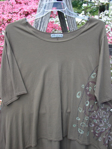 Barclay Hi Low Top Side Art Curly Cue Bark Size 1: An olive-gray tunic with asymmetrical draping, wide rounded neckline, and teal-brown abstract print, displayed against a rustic backdrop.