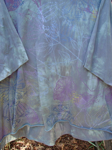 Barclay Flutter Collar Essential Tee Mood Garden Mottled Gray Grass OSFA draped outdoors, showcasing its semi-sheer pastel-dyed fabric with botanical motifs, scalloped edges, and a flowing silhouette.
