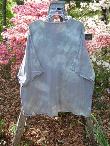 Barclay Flutter Collar Essential Tee Mood Garden Mottled Gray Grass OSFA, draped over a wooden ladder, showcases its boxy shape, rounded flutter neckline, and raw-edged dolman sleeves amidst a floral backdrop.