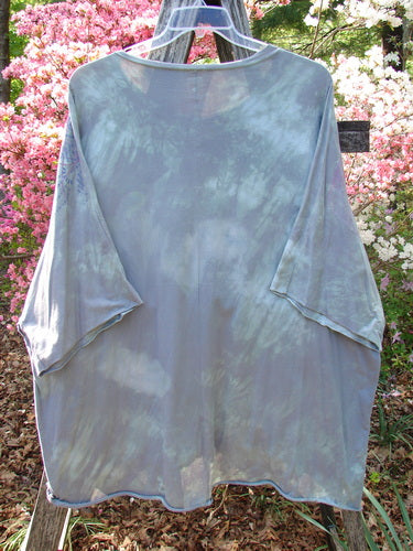 Barclay Flutter Collar Essential Tee Mood Garden Mottled Gray Grass OSFA displayed on a hanger, highlighting its flutter neckline, raw edge dolman sleeves, and hi-low hemline against a garden backdrop.