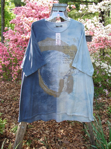 Barclay NWT Art Tee Center Script Bird Mottled Ink Sky Bronze OSFA displayed on a hanger, showcasing its abstract circular design and tunic length against a natural garden backdrop.