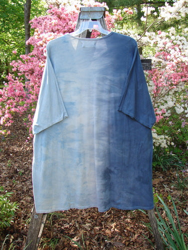 Barclay NWT Art Tee Center Script Bird Mottled Ink Sky Bronze OSFA: A faded blue tunic with drop shoulders and loose three-quarter sleeves, drying on a wooden ladder amidst a garden setting.