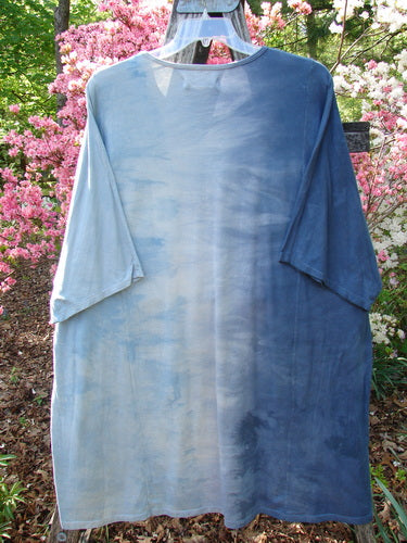Barclay NWT Art Tee Center Script Bird Mottled Ink Sky Bronze OSFA hanging outdoors, showcasing its loose fit, three-quarter sleeves, and rounded neckline in a garden setting with vibrant blooms.
